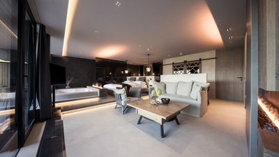 L’esclusività in foto: il nostro chalet in Alto Adige di lusso Area soggiorno moderna con camino, divano e letto matrimoniale sullo sfondo