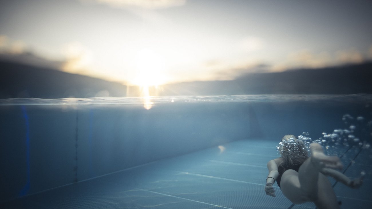 Persona che nuota sott'acqua in piscina al tramonto