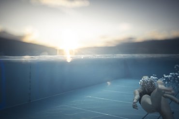 Person swimming underwater in pool at sunset
