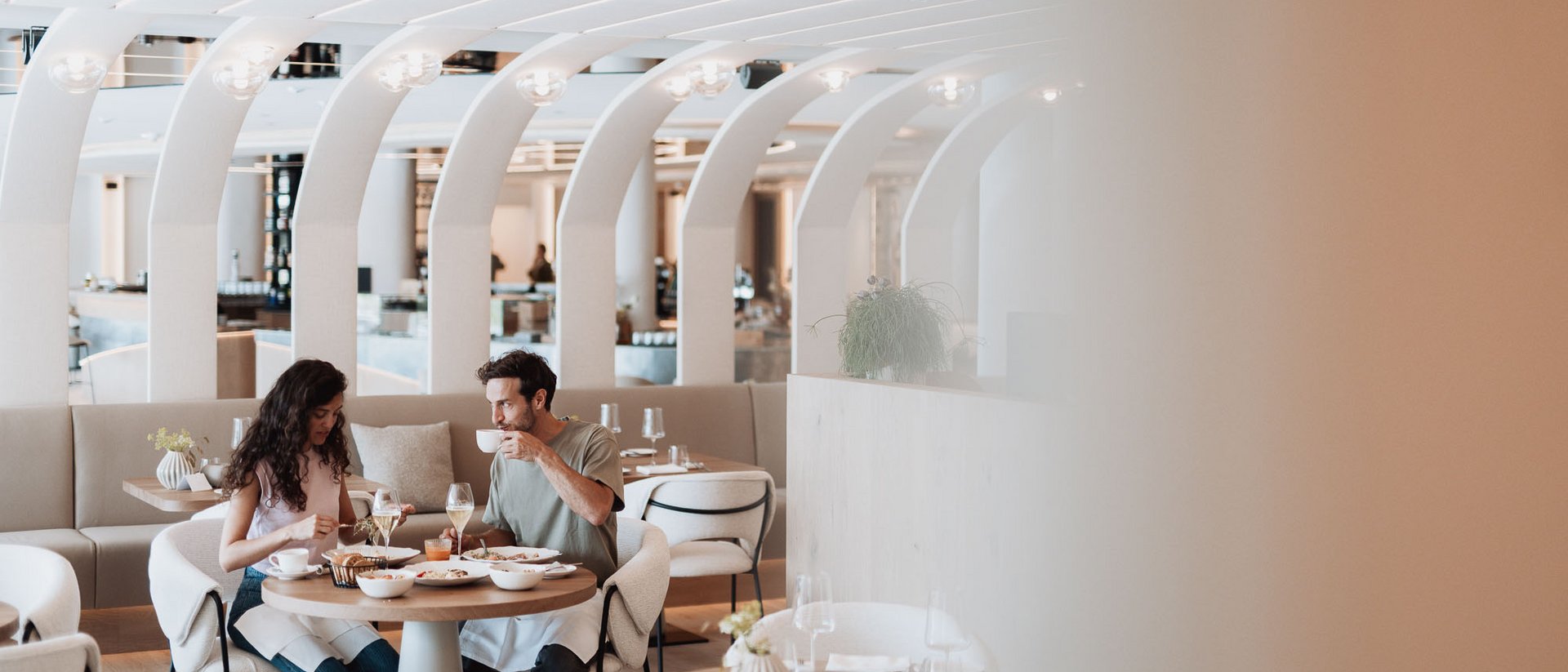 Die Heimat des Strahlens: Ihr Wellnesshotel in Südtirol Paar isst und trinkt in modernem Restaurant mit gebogenen weißen Deckenbögen