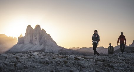 Hikers on rocky terrain with Dolomites mountains at sunset