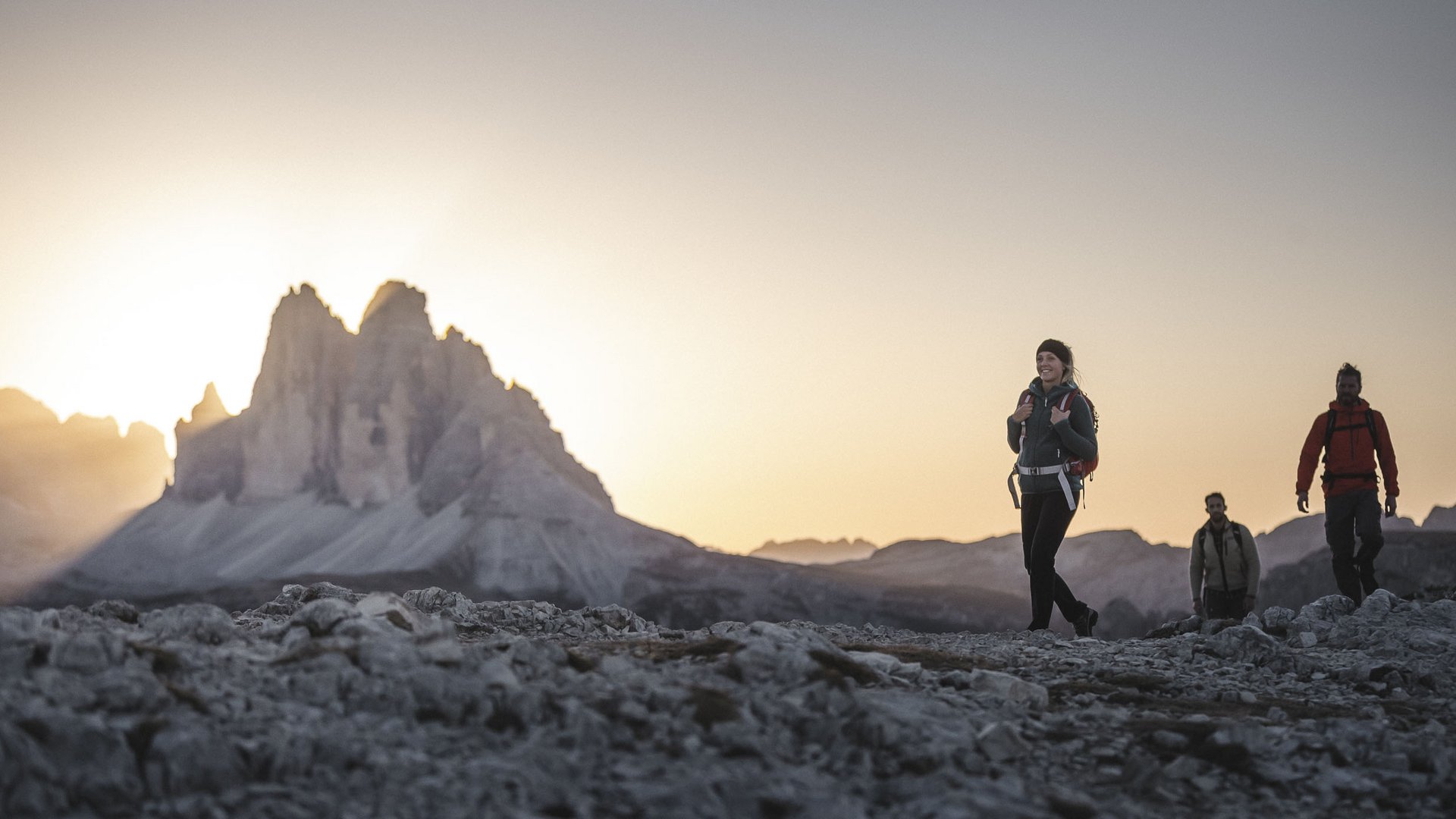 Hikers on rocky terrain with Dolomites mountains at sunset