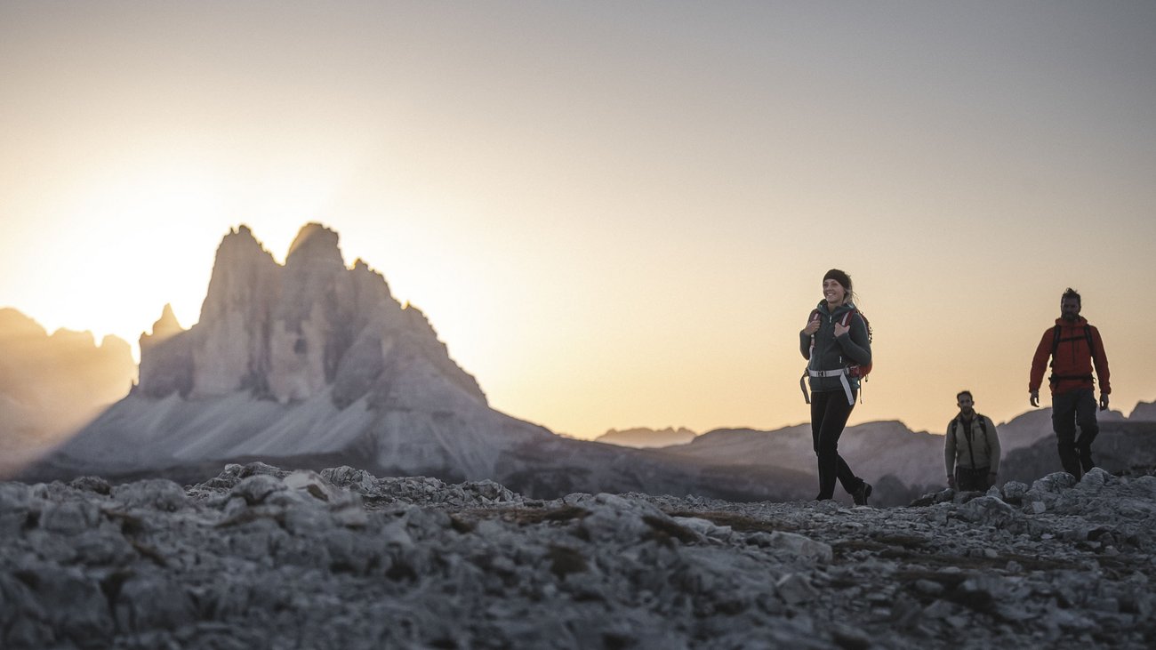 Escursionisti su terreno roccioso con le Dolomiti al tramonto