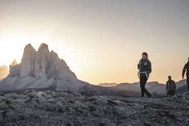 Escursionisti su terreno roccioso con le Dolomiti al tramonto