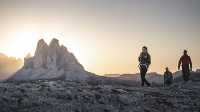 Escursionisti su terreno roccioso con le Dolomiti al tramonto
