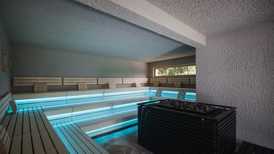 Sauna moderna con panche in legno illuminate e forno a pietra