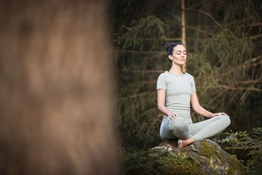 Donna in posa di yoga medita su una roccia coperta di muschio nella foresta