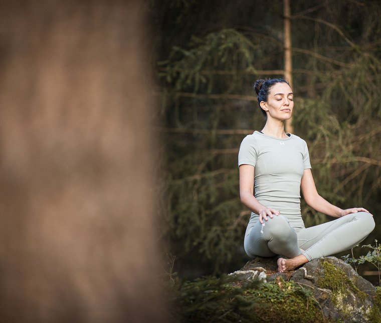 Eine regenerierende Auszeit vor Weihnachten Frau meditiert im Yoga-Sitz auf moosbedecktem Felsen im Wald