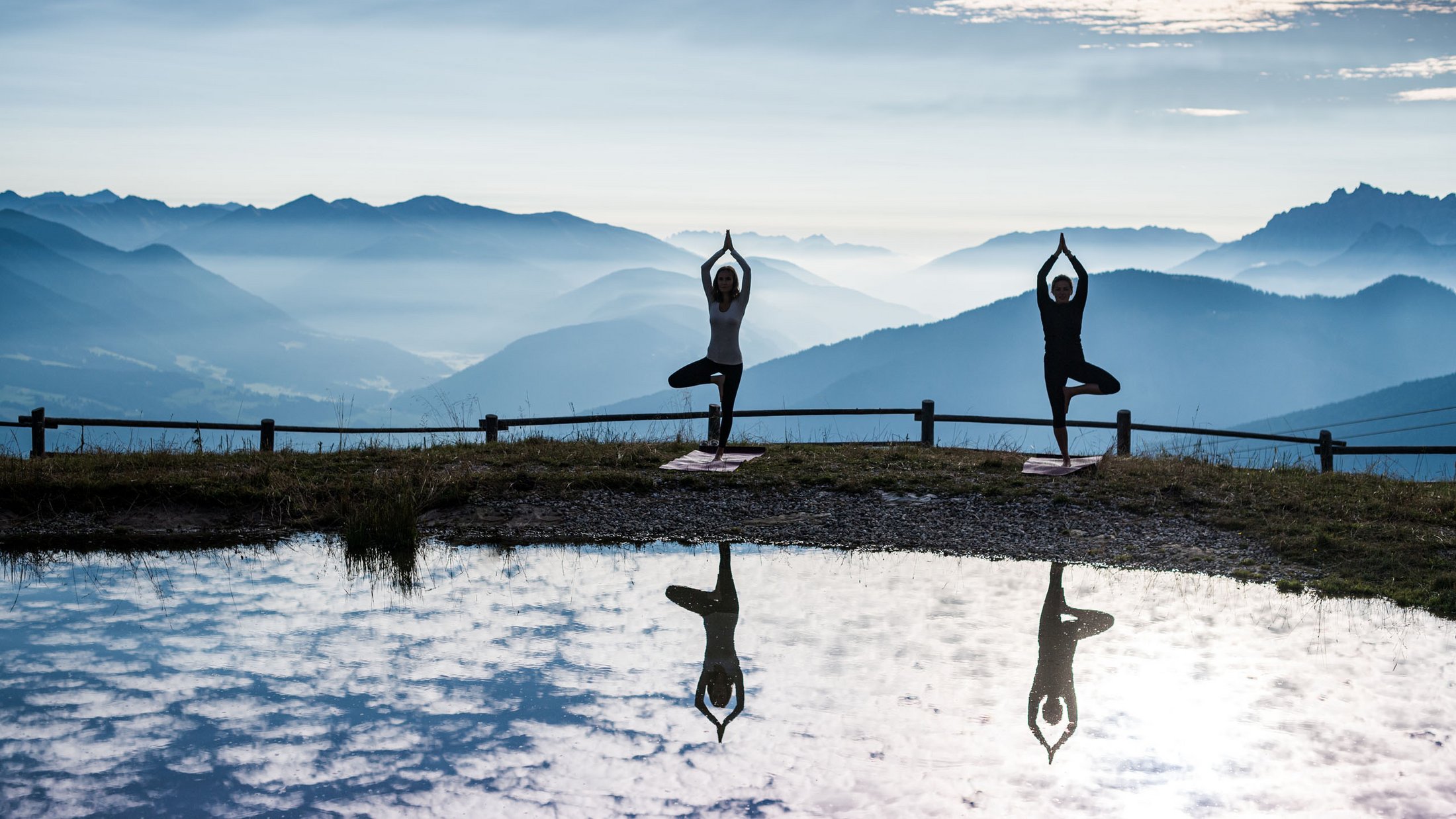 Due persone fanno yoga con vista montana e riflesso sull'acqua