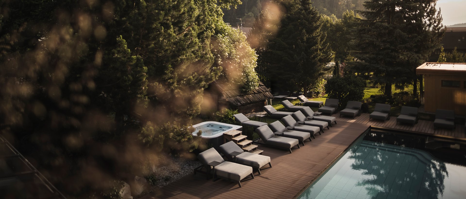 Piscina con lettini e vasca idromassaggio in un resort montano boscoso al tramonto