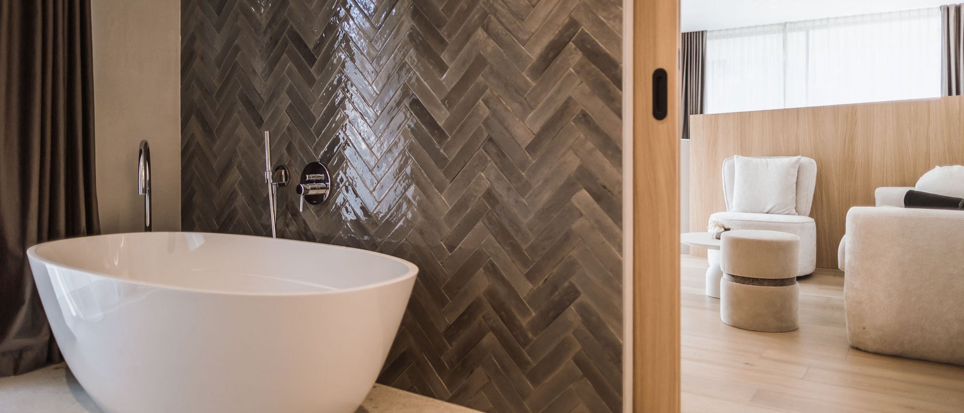 Vasca da bagno autonoma davanti a parete di piastrelle scure accanto a soggiorno luminoso