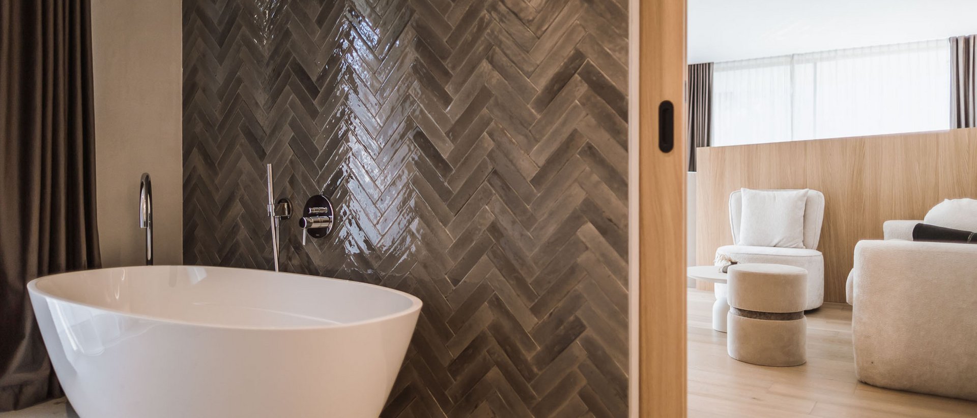 Vasca da bagno autonoma davanti a parete di piastrelle scure accanto a soggiorno luminoso