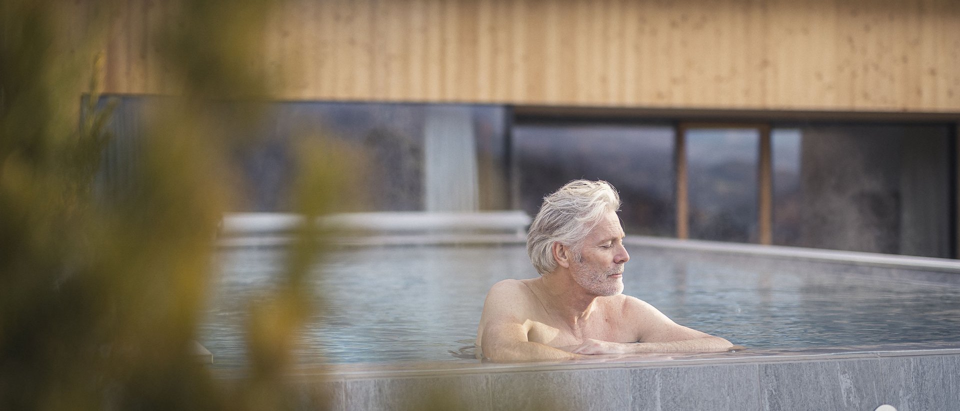 Older man relaxing in an outdoor pool at a modern house