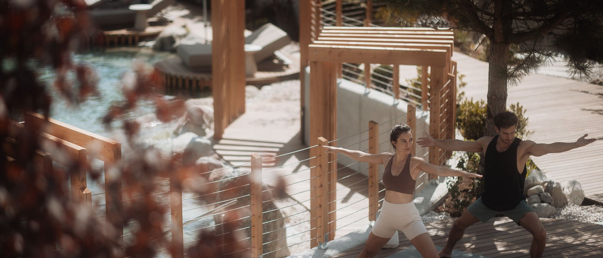 Winklerhotels: relax negli hotel per yoga in Alto Adige Due persone fanno yoga su una terrazza in legno vicino a una piscina