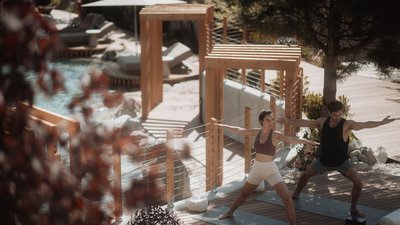Photos from your hotel in Pfalzen in Val Pusteria/Pustertal Two people doing yoga on a wooden deck beside a pool