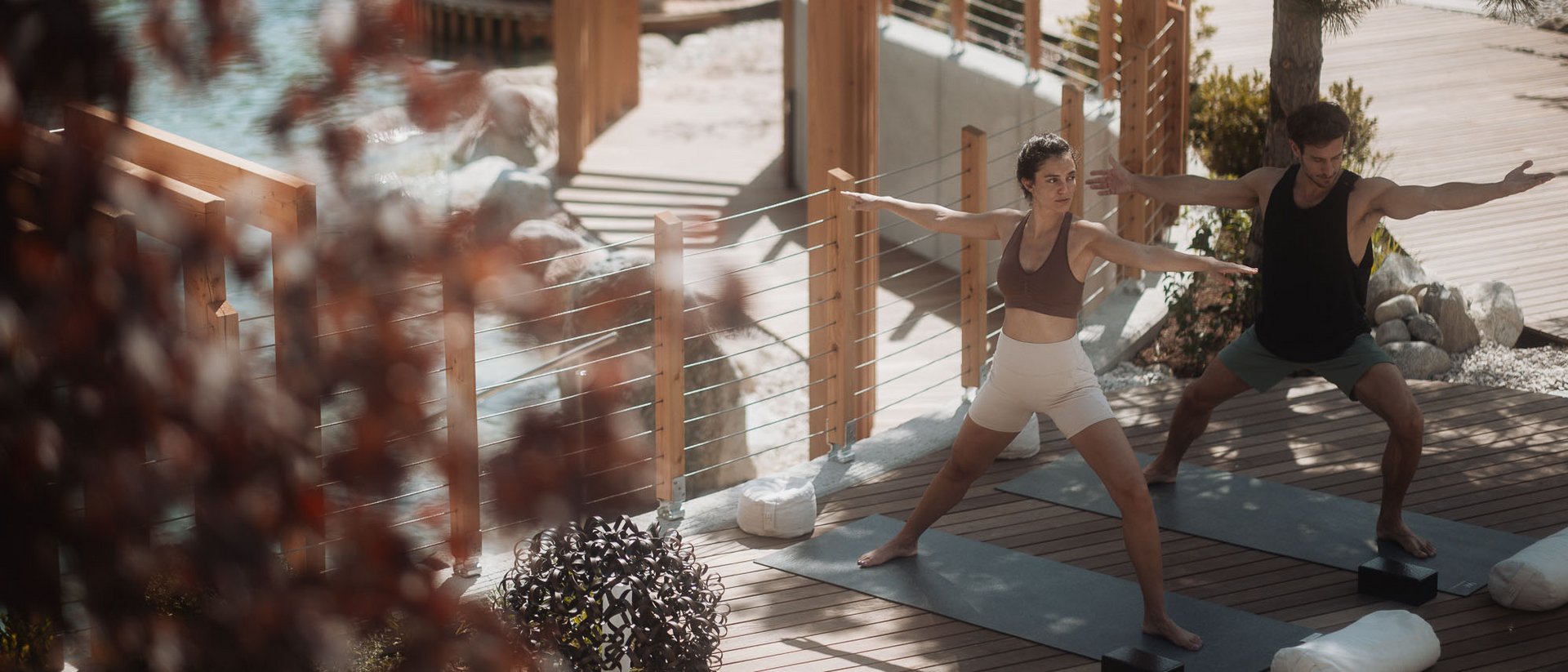 Zwei Menschen machen Yoga auf einer Holzterrasse neben einem Pool