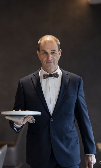 Waiter in dark suit with wooden bow tie serving food in upscale restaurant