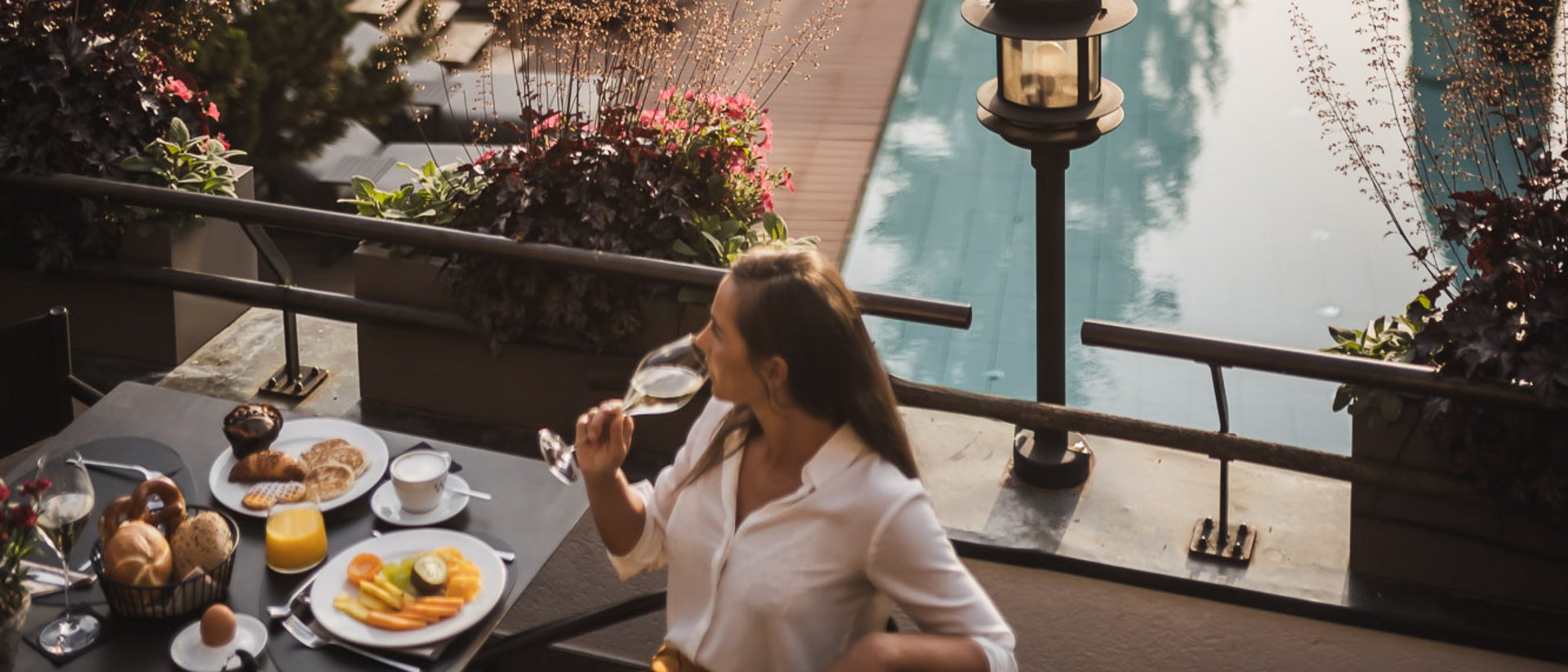 Il benessere nasce qui: il nostro hotel in Val Pusteria Donna beve vino a colazione con piscina e alberi sullo sfondo