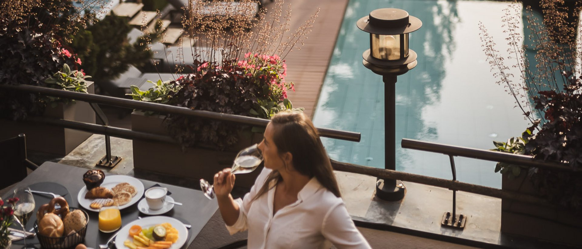 Woman drinking wine at breakfast by pool with trees in background