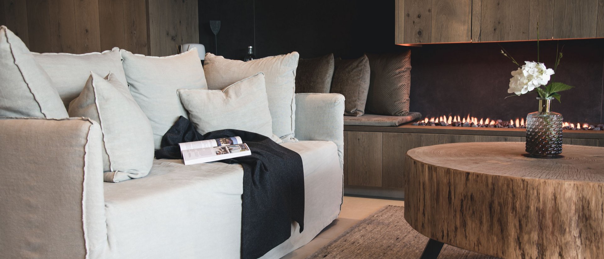 Gemütliches Wohnzimmer mit Sofakissen, Kaminfeuer und Holztisch mit Vase