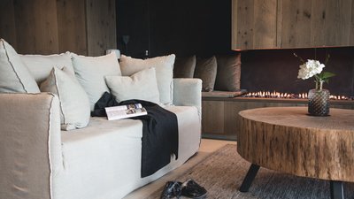 L’esclusività in foto: il nostro chalet in Alto Adige di lusso Soggiorno accogliente con divano, camino e tavolo in legno con vaso
