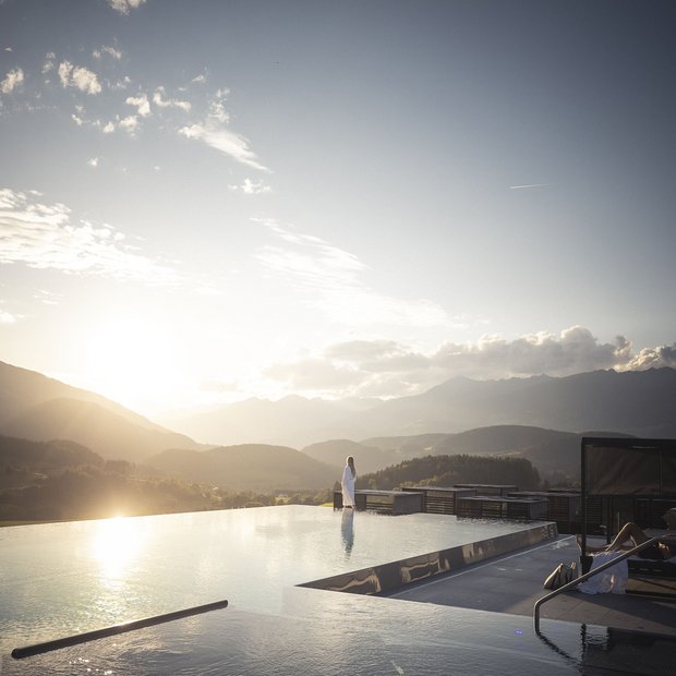 Persona in accappatoio alla piscina a sfioro al tramonto con vista sulle montagne