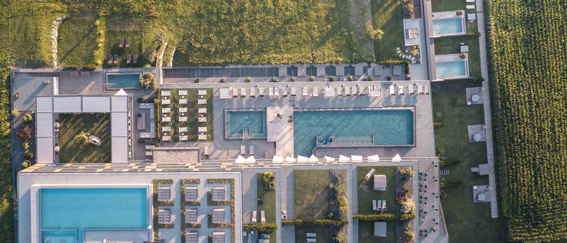 Your source of enrichment: our hotel at Mt Plan de Corones Aerial view of a resort with several pools, sun loungers and adjacent fields