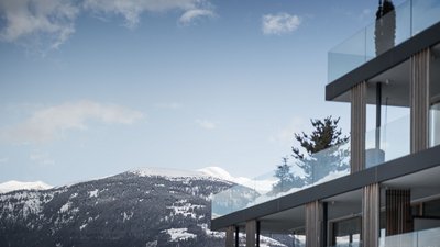 Facciata di edificio moderno con balconi in vetro davanti a paesaggio montano innevato