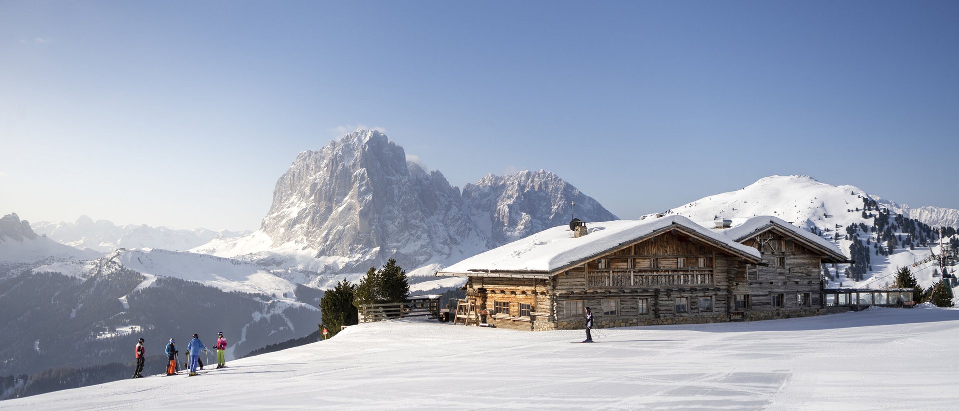 Skiers in front of snowy mountain lodge in sunny Alps