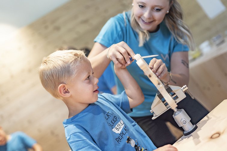Instructor helping child saw a piece of wood in workshop