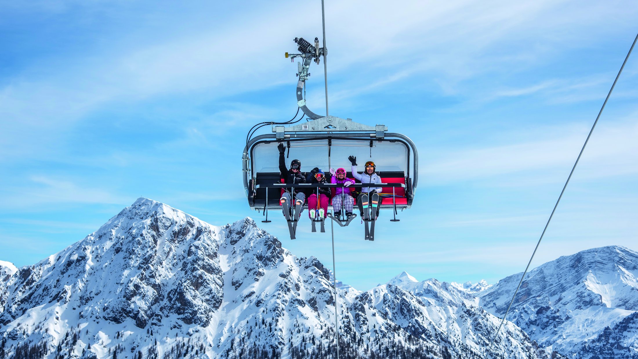 Vier Skifahrer auf einem Sessellift vor schneebedeckten Bergen