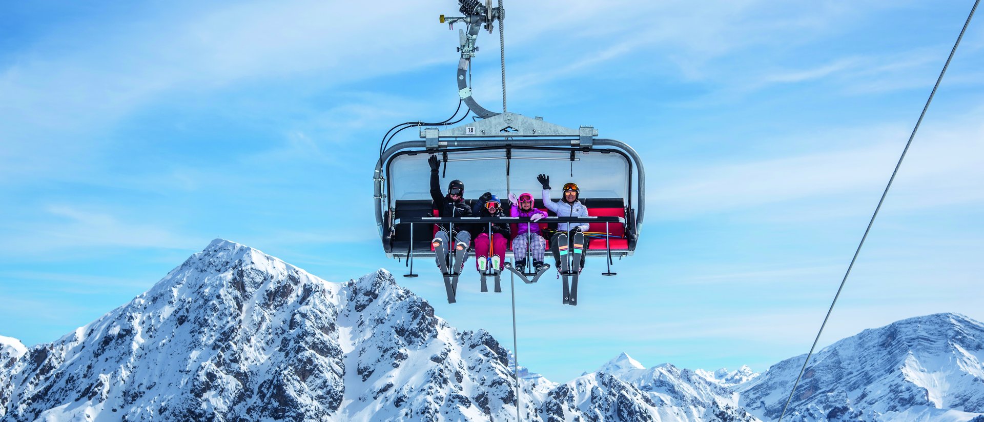 Vier Skifahrer auf einem Sessellift vor schneebedeckten Bergen