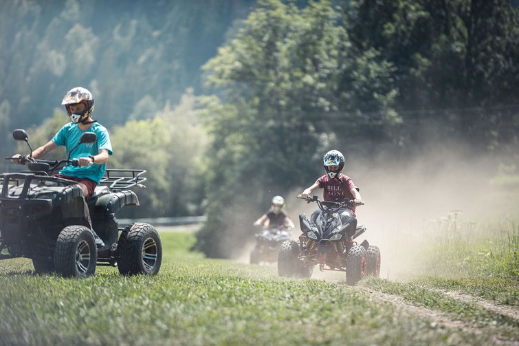 Tre persone guidano quad su un prato polveroso