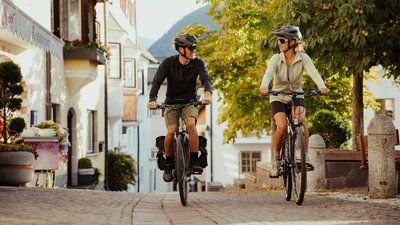 Due persone in bicicletta su una strada acciottolata in una città soleggiata