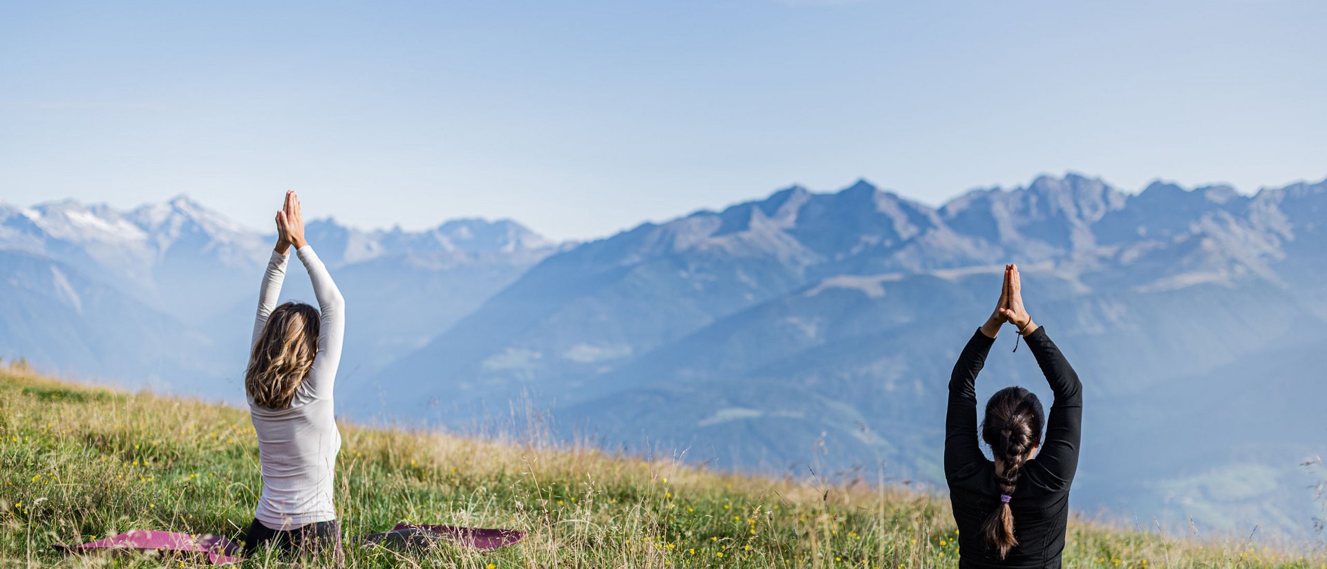 Zwei Frauen praktizieren Yoga auf einer Wiese mit Bergblick