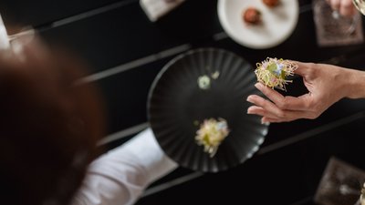 L’esclusività in foto: il nostro chalet in Alto Adige di lusso Mano che tiene un piccolo antipasto gourmet con fiori commestibili sopra un piatto nero