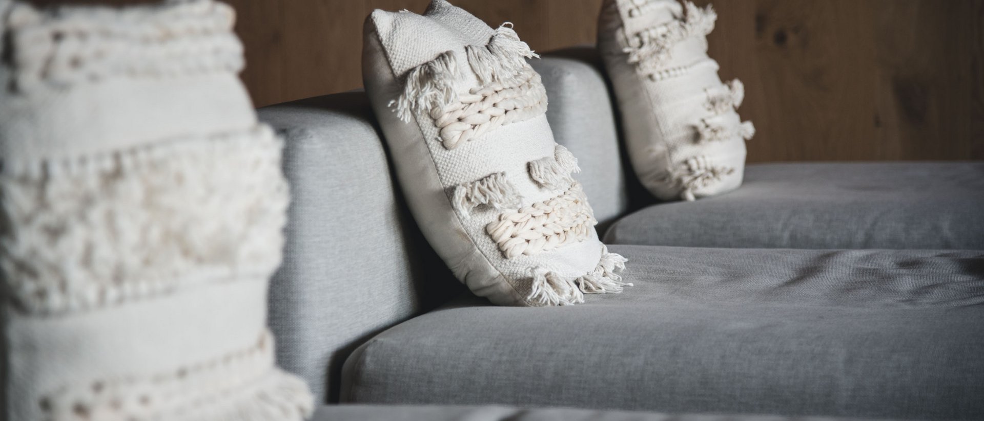 Light gray sofa with three white decorative pillows against a wooden wall