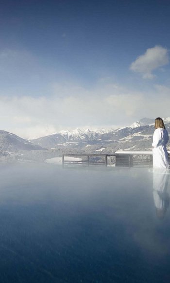 Woman in bathrobe by heated outdoor pool overlooking snowy mountains