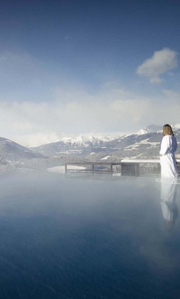 Donna in accappatoio vicino a piscina riscaldata all'aperto con vista sulle montagne innevate