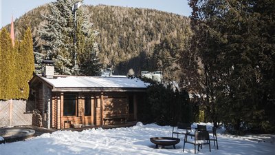 Casa in legno con giardino innevato e sedie davanti a collina boscosa