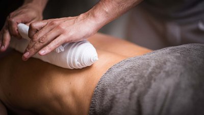 Mani che avvolgono un panno caldo sulla schiena durante un massaggio