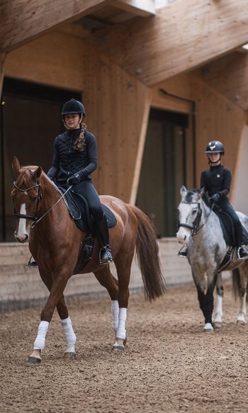 I vostri hotel in Alto Adige: qui dove tutto è possibile Lezione di equitazione con tre bambini a cavallo e un istruttore in una scuderia