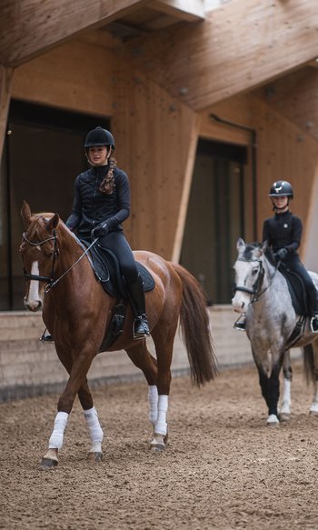 Reitstunde mit drei Kindern auf Pferden und einem Trainer in einer Halle