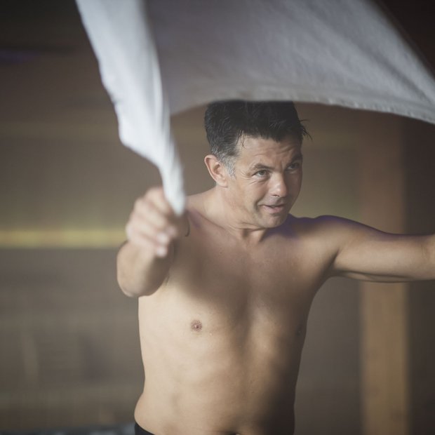 Uomo senza maglietta che sventola un panno bianco in una stanza fumosa