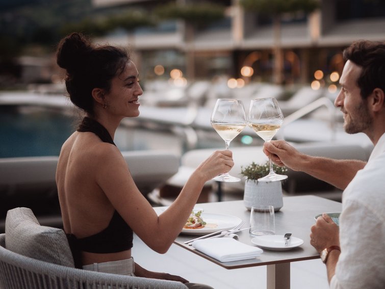 Paar stößt mit Weißwein an auf Terrasse bei Sonnenuntergang.