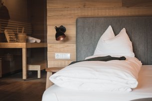 Cozy single bed with white bedding next to wooden sauna