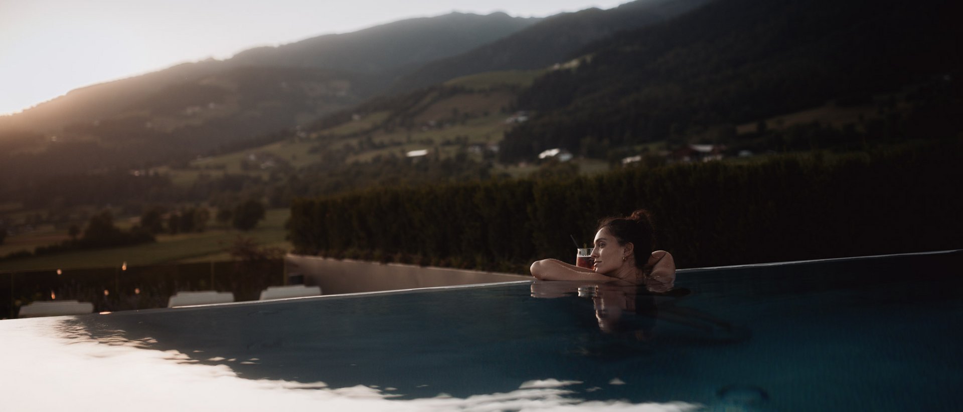 Die Heimat des Strahlens: Ihr Wellnesshotel in Südtirol Frau entspannt im Infinity-Pool mit Bergblick bei Sonnenuntergang