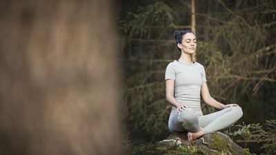 Donna che medita seduta su una roccia nella foresta verde