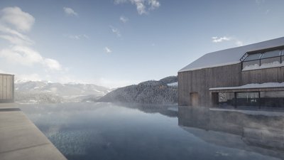 Piscina a sfioro con vista sulle montagne e casa di legno innevata sotto cielo azzurro