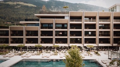 Modernes Hotel mit Pool und Liegestühlen vor bewaldetem Berg